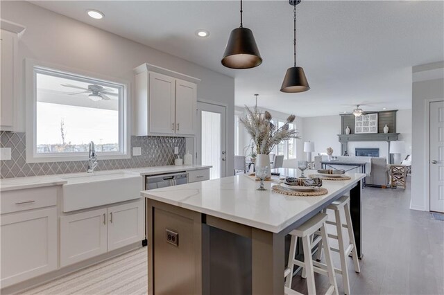 kitchen featuring white cabinets, a sink, a large fireplace, a ceiling fan, and decorative backsplash