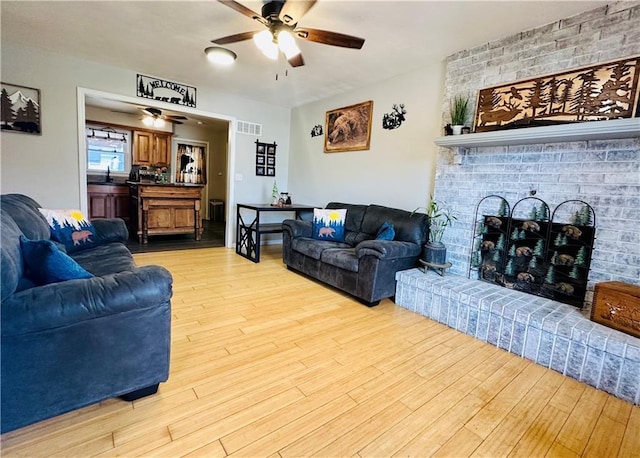 living area with visible vents, light wood finished floors, ceiling fan, and a fireplace