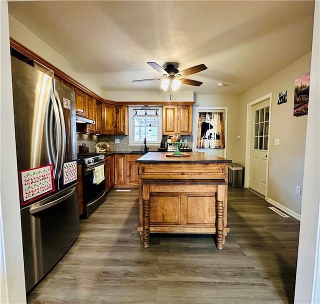 kitchen featuring ceiling fan, freestanding refrigerator, dark wood-type flooring, under cabinet range hood, and range with gas cooktop