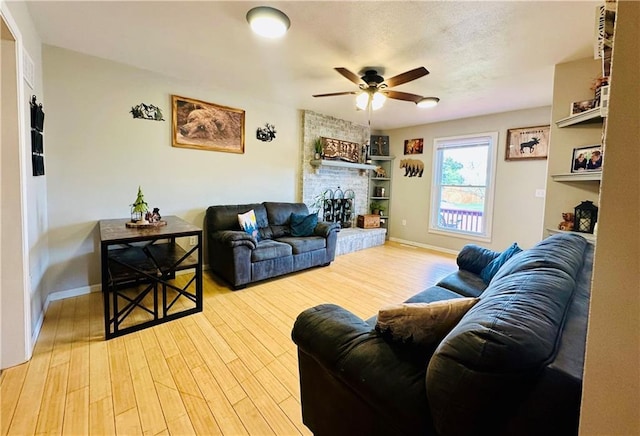 living room with baseboards, a ceiling fan, a brick fireplace, and wood finished floors