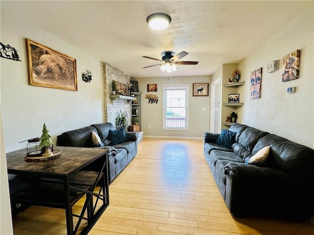living room featuring baseboards, light wood-type flooring, a textured ceiling, built in shelves, and a ceiling fan