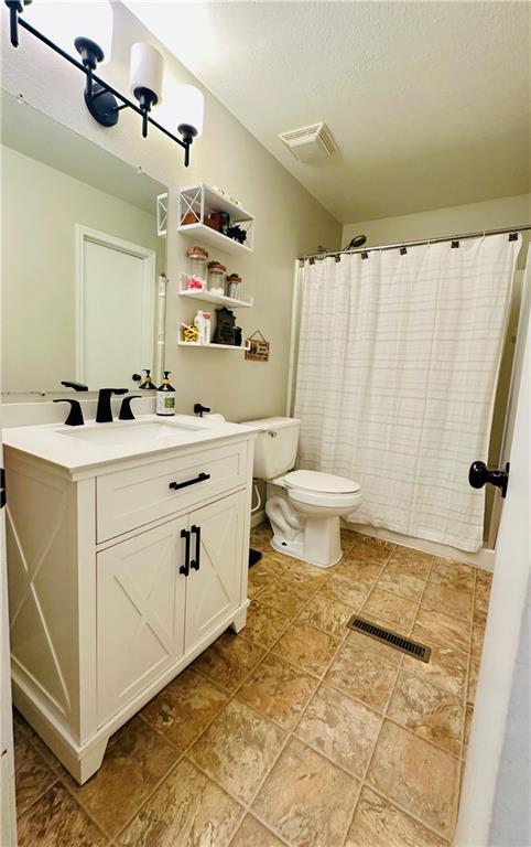 full bathroom with visible vents, stone finish flooring, toilet, and vanity