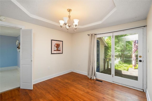 spare room with a chandelier, a raised ceiling, wood finished floors, baseboards, and a water view