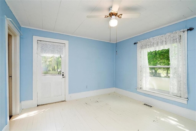 empty room featuring plenty of natural light, wood finished floors, ornamental molding, a ceiling fan, and baseboards