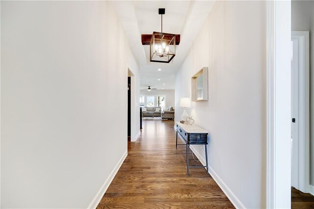 corridor with baseboards, dark wood finished floors, and a notable chandelier