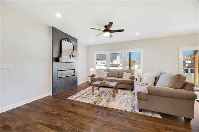 living room featuring a tiled fireplace, a ceiling fan, baseboards, and wood finished floors