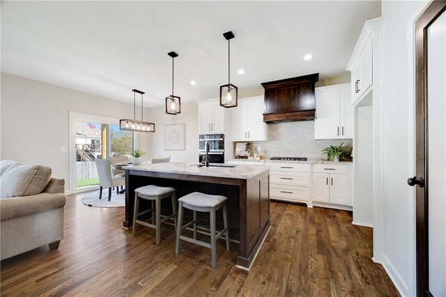 kitchen featuring decorative backsplash, premium range hood, dark wood-style floors, white cabinets, and a sink