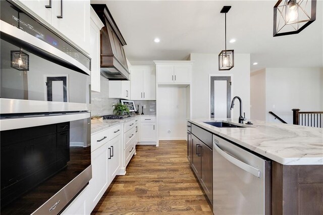 kitchen with appliances with stainless steel finishes, wood finished floors, a sink, recessed lighting, and white cabinetry
