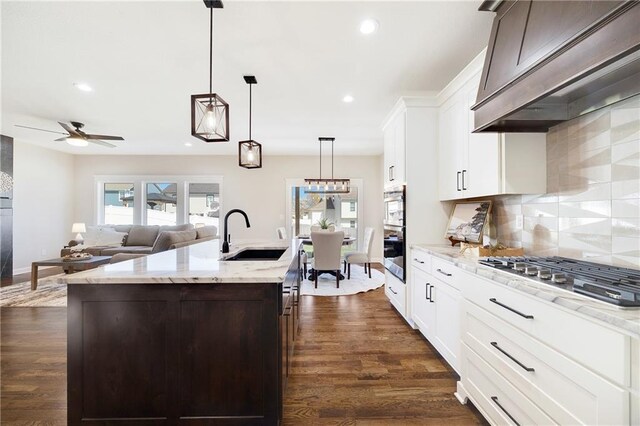 kitchen featuring decorative backsplash, light stone countertops, premium range hood, a sink, and stainless steel appliances