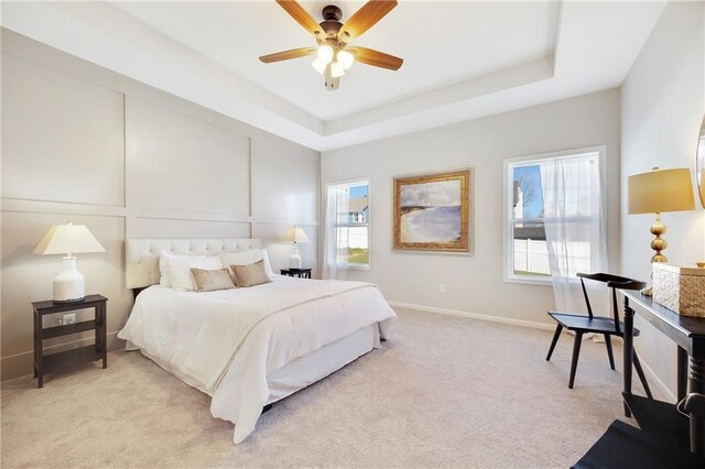 bedroom featuring a raised ceiling, baseboards, light carpet, and a ceiling fan