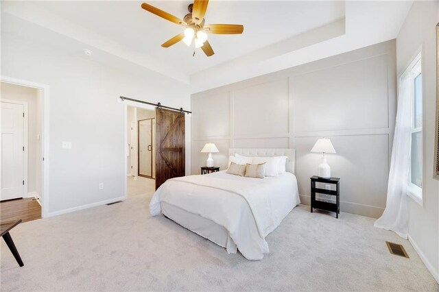 bedroom featuring a ceiling fan, visible vents, a barn door, baseboards, and carpet flooring