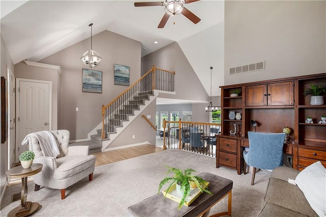 living area with a ceiling fan, light carpet, high vaulted ceiling, and a chandelier