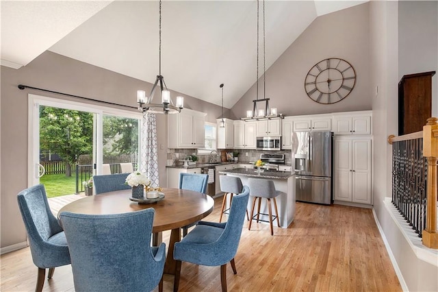 dining area with a chandelier, high vaulted ceiling, light wood-style floors, and baseboards