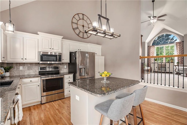 kitchen with appliances with stainless steel finishes, light wood finished floors, backsplash, high vaulted ceiling, and white cabinetry