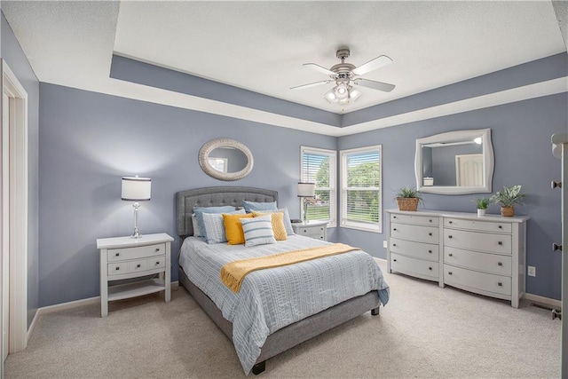 bedroom featuring light colored carpet, baseboards, a tray ceiling, and ceiling fan