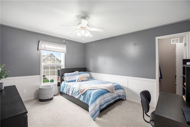 carpeted bedroom with a wainscoted wall and a ceiling fan