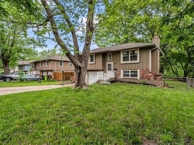 bi-level home featuring fence, a chimney, driveway, and a front lawn