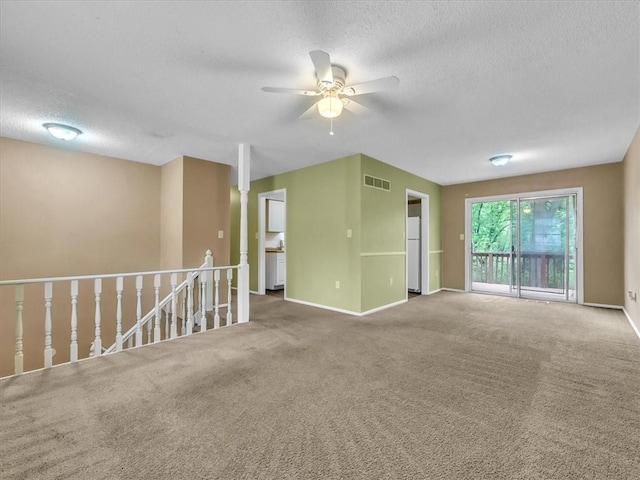 unfurnished room with carpet flooring, a textured ceiling, a ceiling fan, baseboards, and visible vents