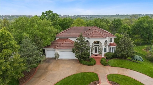 mediterranean / spanish-style home with a tile roof, an attached garage, a front yard, driveway, and a forest view
