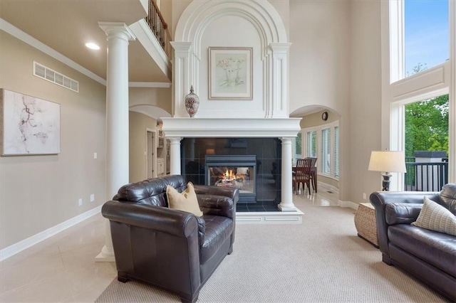 living room featuring arched walkways, ornate columns, baseboards, a tiled fireplace, and a high ceiling