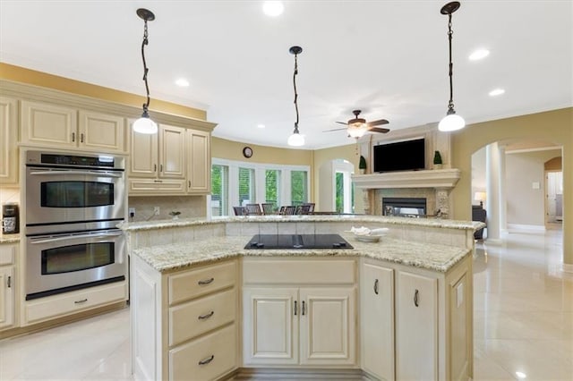 kitchen with cream cabinetry, arched walkways, double oven, a ceiling fan, and ornamental molding