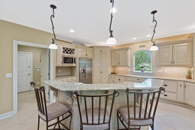 kitchen with appliances with stainless steel finishes, cream cabinets, a sink, a breakfast bar area, and backsplash