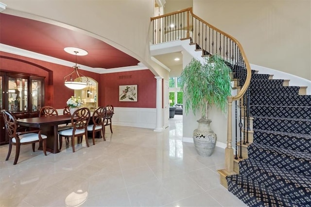 stairway featuring decorative columns, crown molding, arched walkways, a wainscoted wall, and a decorative wall