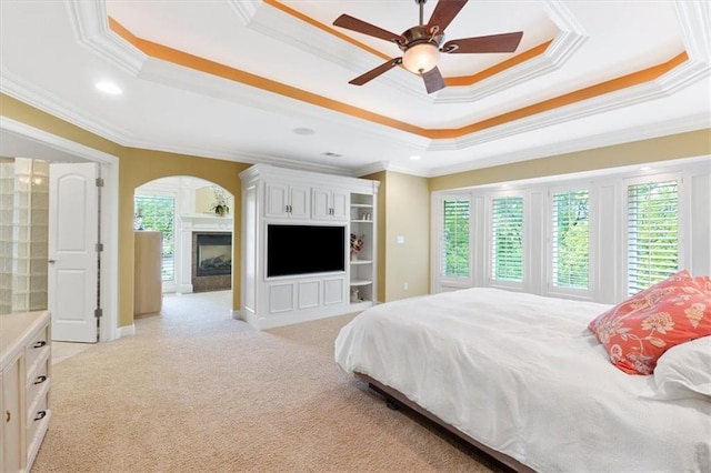 bedroom featuring a tray ceiling, ornamental molding, light carpet, arched walkways, and a fireplace