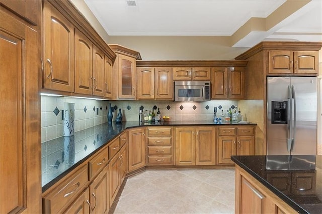 kitchen featuring appliances with stainless steel finishes, dark stone counters, brown cabinetry, decorative backsplash, and glass insert cabinets