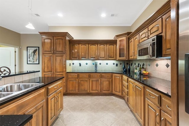 kitchen featuring stainless steel microwave, decorative backsplash, pendant lighting, brown cabinets, and crown molding