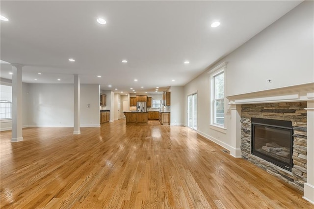 875 Clearview Dr, Lansing, KS 66043 - unfurnished living room featuring light wood-style floors, healthy amount of natural light, recessed lighting, a stone fireplace, and ornate columns