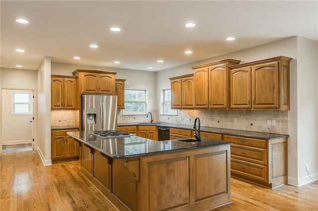 875 Clearview Dr, Lansing, KS 66043 - kitchen with stainless steel appliances, an island with sink, brown cabinetry, backsplash, and light wood-style floors