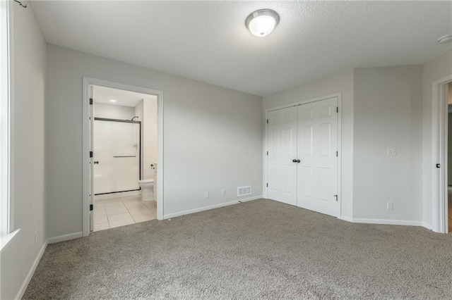 875 Clearview Dr, Lansing, KS 66043 - unfurnished bedroom featuring carpet, a closet, ensuite bathroom, a textured ceiling, and tile patterned floors