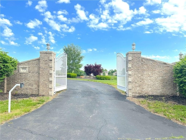 view of asphalt driveway featuring street lights, a gate, and a gated entry