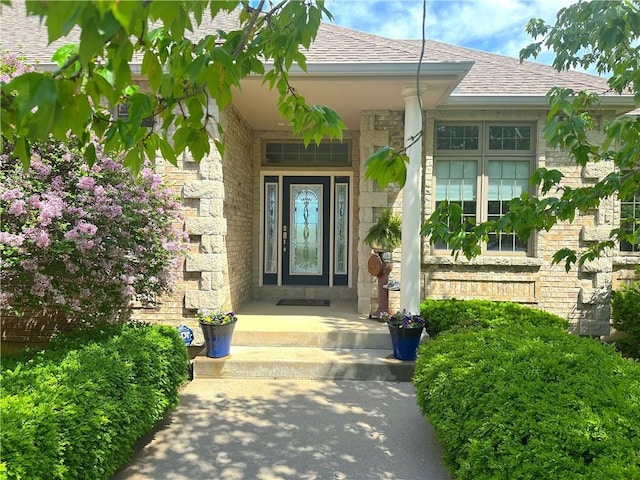 doorway to property featuring a shingled roof and stone siding