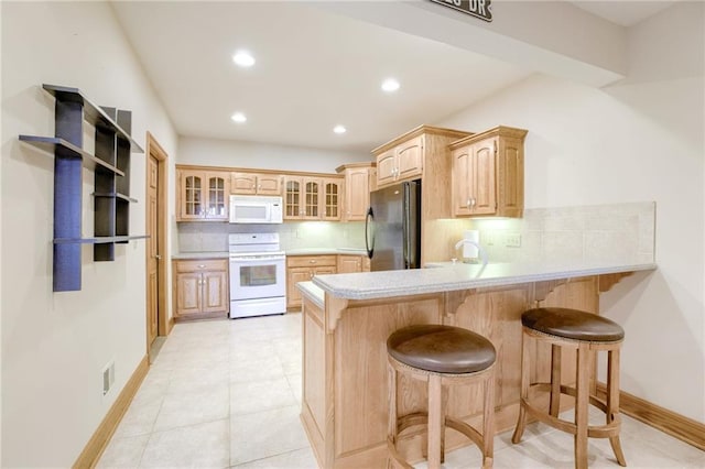 kitchen featuring white appliances, a peninsula, a kitchen bar, backsplash, and recessed lighting