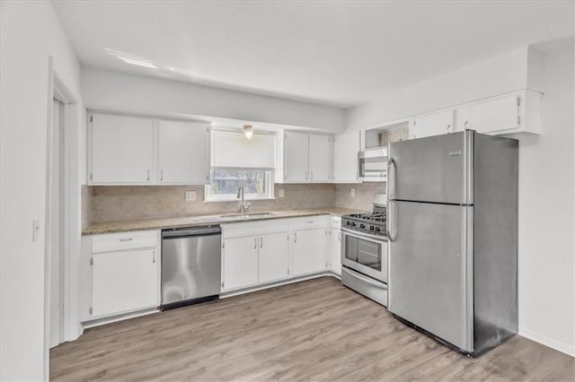 705 NW 88th Ter, Kansas City, MO 64155 - kitchen featuring appliances with stainless steel finishes, tasteful backsplash, a sink, light wood finished floors, and white cabinetry