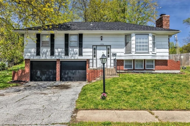 split foyer home with an attached garage, brick siding, aphalt driveway, a front yard, and a chimney