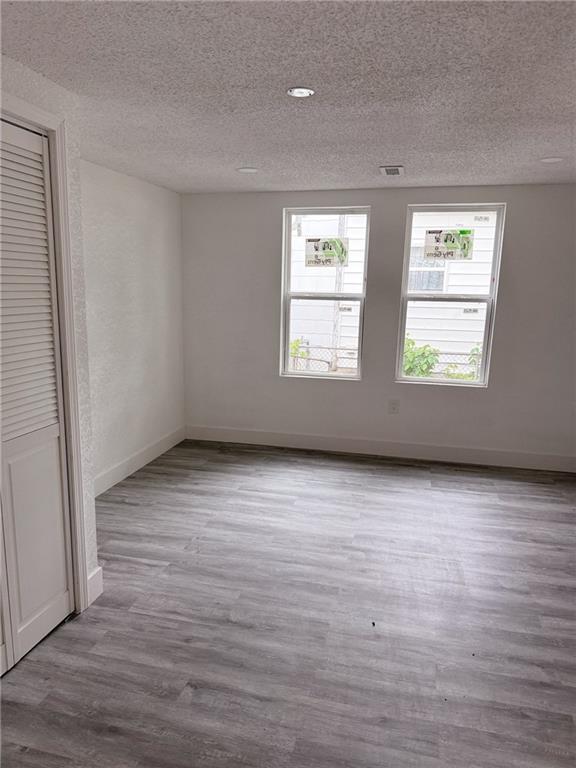 unfurnished bedroom featuring a textured ceiling, wood finished floors, and multiple windows