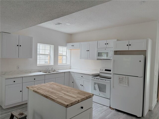 kitchen with a sink, white cabinets, butcher block counters, white appliances, and light wood-style flooring