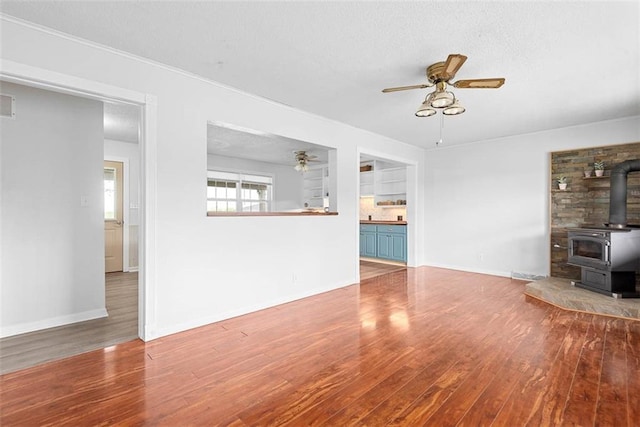 588 NW 105th Rd, Centerview, MO 64019 - unfurnished living room featuring a wood stove, ceiling fan, wood finished floors, and baseboards