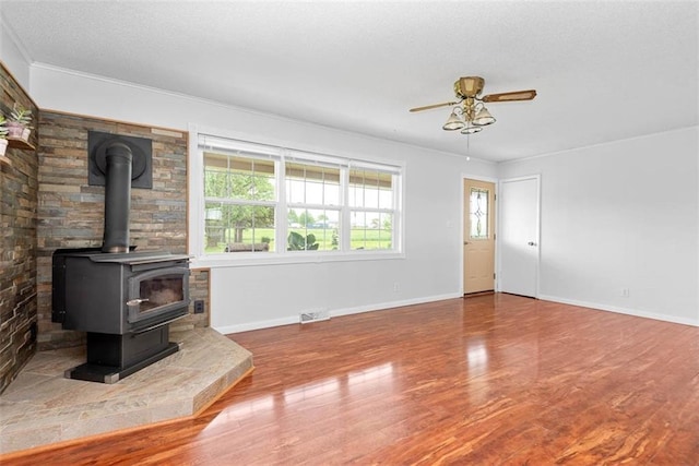 588 NW 105th Rd, Centerview, MO 64019 - unfurnished living room with a wood stove, wood finished floors, a ceiling fan, baseboards, and a textured ceiling