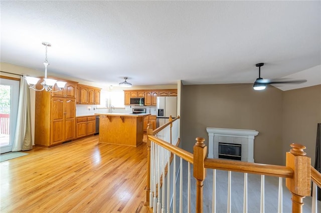 3616 Anchor Ct, Blue Springs, MO 64015 - kitchen with appliances with stainless steel finishes, a tiled fireplace, a kitchen island, a chandelier, and light wood-type flooring