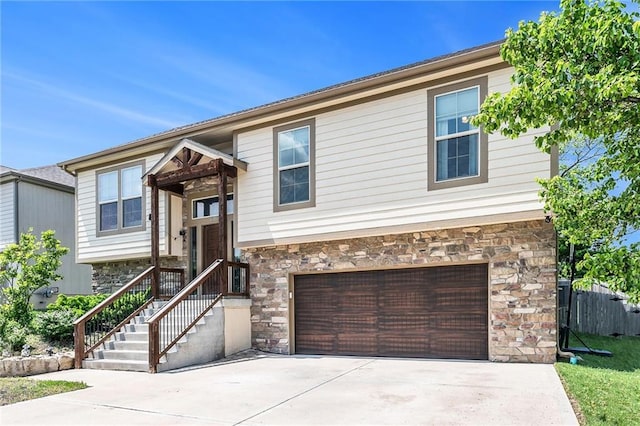 raised ranch with stone siding, concrete driveway, a garage, and fence