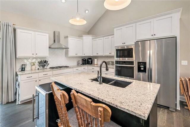 kitchen featuring stainless steel appliances, wall chimney exhaust hood, a sink, dark wood-style flooring, and high vaulted ceiling