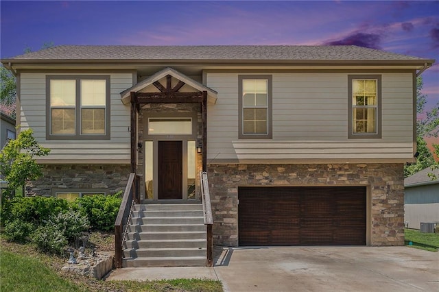 split foyer home featuring stone siding, a garage, and driveway