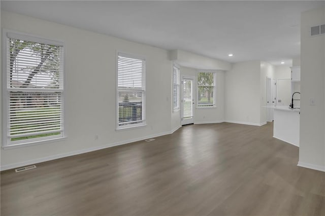unfurnished living room with visible vents, dark wood-style flooring, baseboards, recessed lighting, and a sink