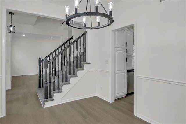 staircase with baseboards, wood finished floors, and a notable chandelier