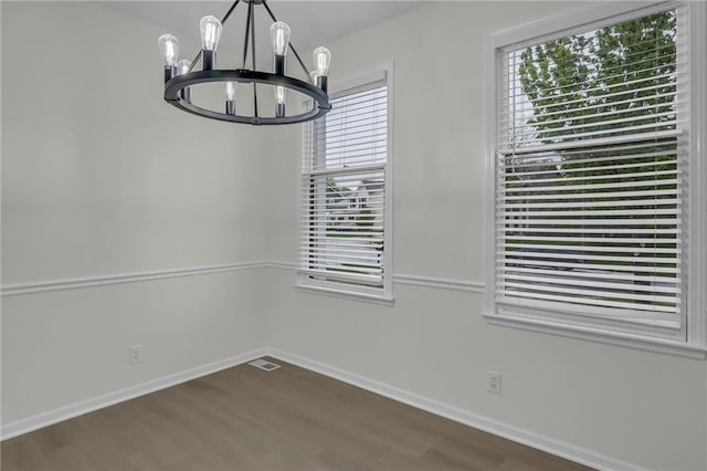 unfurnished dining area with baseboards, visible vents, wood finished floors, and a notable chandelier