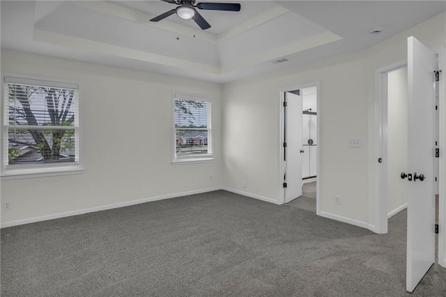 unfurnished bedroom with baseboards, a tray ceiling, dark colored carpet, and visible vents
